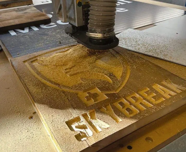 CNC router carving the Skybreak logo and lettering into a wood sign blank